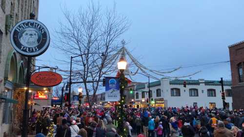 A large crowd gathers in a festive downtown area, with holiday decorations and a pub sign visible.