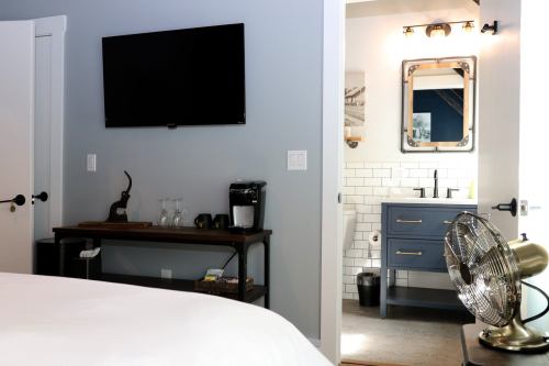 A modern bedroom with a TV, coffee station, and a bathroom featuring a sink and mirror.