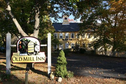 A charming yellow inn surrounded by trees, featuring a sign that reads "The Old Mill Inn" in a picturesque setting.