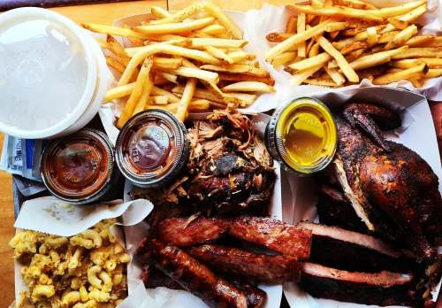 A spread of barbecue featuring pulled pork, ribs, smoked chicken, fries, and macaroni and cheese with sauces on the side.