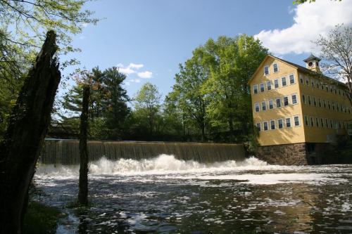 A yellow building beside a waterfall, surrounded by lush green trees and a clear blue sky.