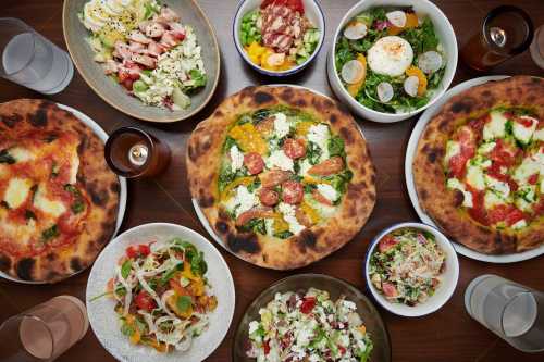 A variety of pizzas and salads arranged on a table, showcasing colorful ingredients and diverse dishes.