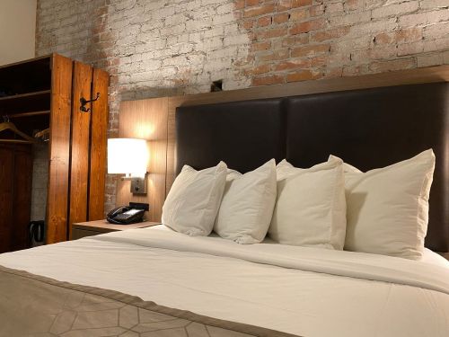 Cozy bedroom with a large bed, fluffy pillows, and exposed brick walls, featuring a wooden wardrobe and bedside lamp.