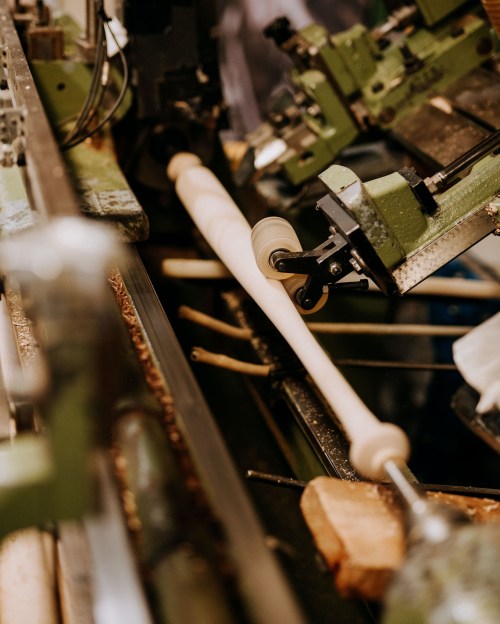 A close-up of a woodworking machine shaping a wooden piece, with tools and machinery in the background.