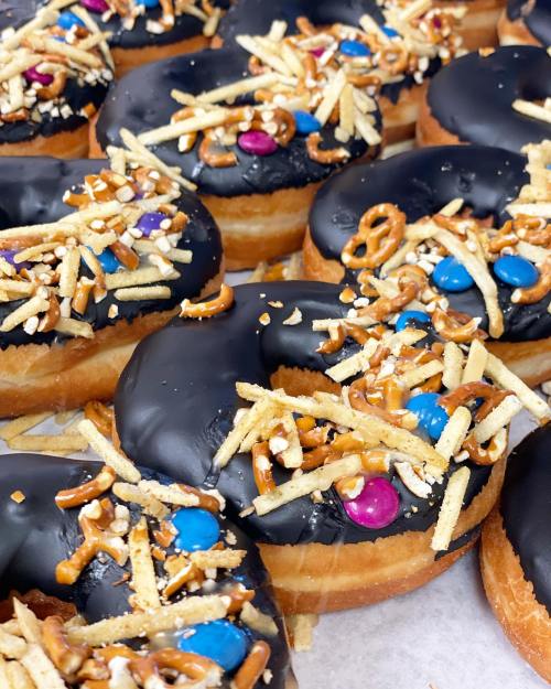 A close-up of chocolate-glazed donuts topped with pretzel pieces and colorful candy.
