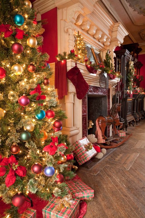 A beautifully decorated Christmas tree beside a festive fireplace, adorned with stockings and wrapped gifts.