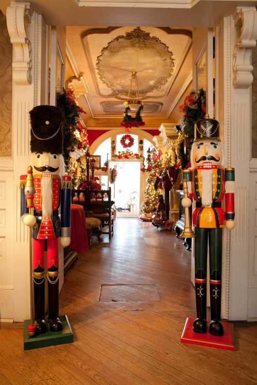 Two colorful nutcracker figures stand at the entrance of a festive, decorated hallway filled with holiday decorations.