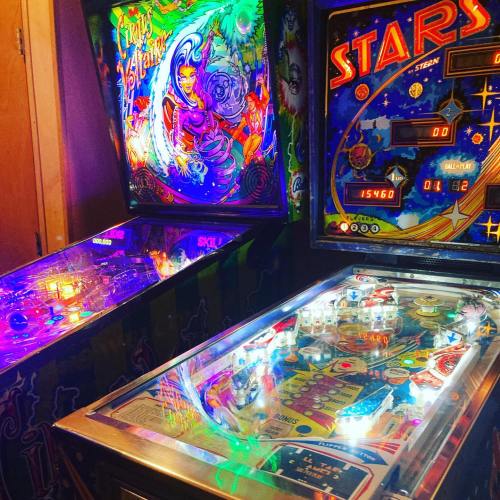 A vibrant arcade with two pinball machines, featuring colorful artwork and illuminated playfields.