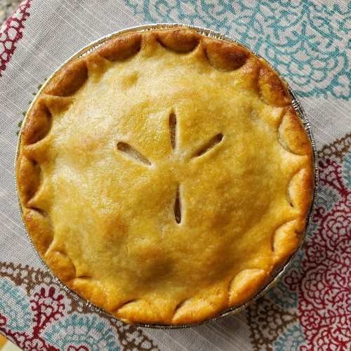 A golden-brown pie with a decorative crust and steam vents, resting on a patterned cloth.