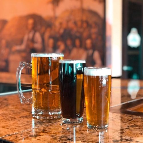 Three glasses of beer in varying colors and sizes on a polished bar counter, with a blurred background.