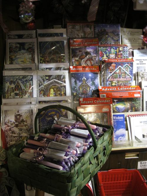 A display of colorful Advent calendars and holiday cards, with a basket of rolled candles in the foreground.