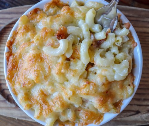 A creamy, cheesy macaroni and cheese dish with a golden, crispy top served in a white bowl.