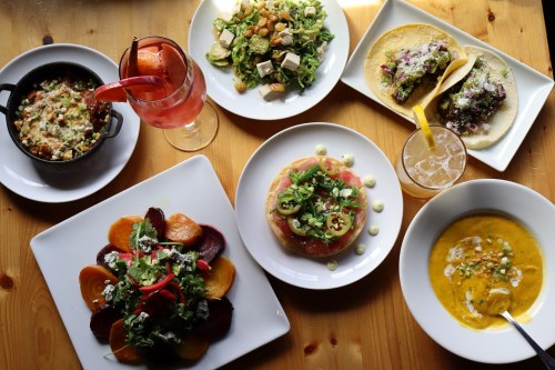 A vibrant spread of dishes including salads, tacos, and colorful appetizers, accompanied by refreshing drinks on a wooden table.