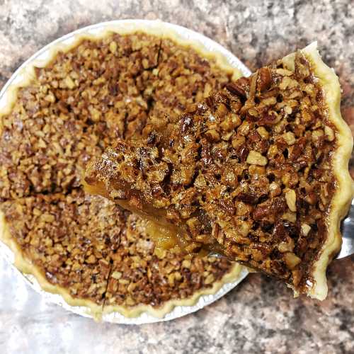 A pecan pie with a slice being lifted out, showcasing a golden filling and a crunchy nut topping.