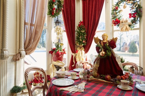 A festive dining table decorated for Christmas, featuring an angel centerpiece and holiday wreaths in a bright room.