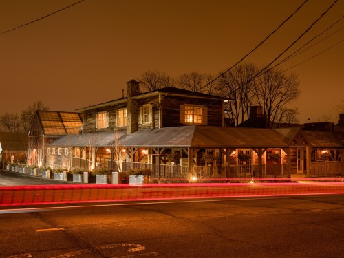 A cozy restaurant with warm lights, surrounded by trees, under a night sky with a hint of orange glow.