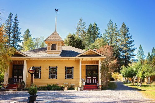 A charming yellow house with a cupola, surrounded by trees and a gravel path, under a clear blue sky.
