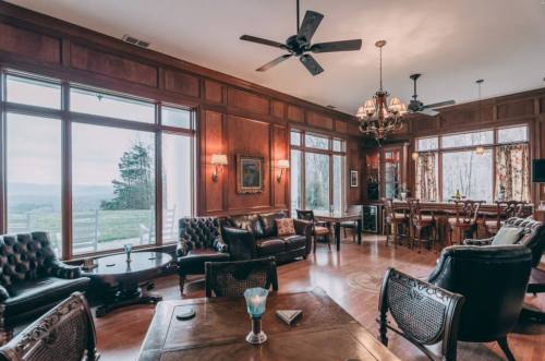 Cozy interior of a room with wooden walls, large windows, elegant furniture, and a scenic view.