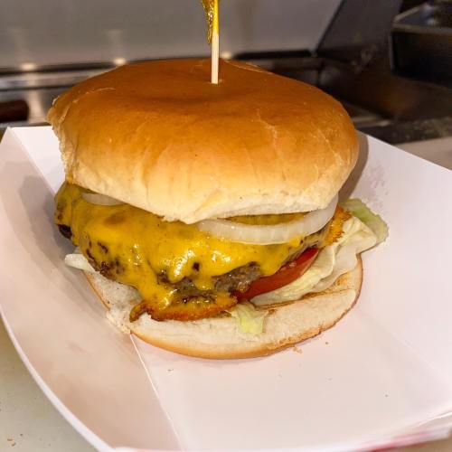 A juicy cheeseburger with melted cheese, lettuce, tomato, and onions, served in a soft bun with a toothpick on top.