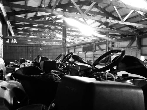 A dimly lit barn interior filled with parked go-karts, showcasing their steering wheels and outlines.
