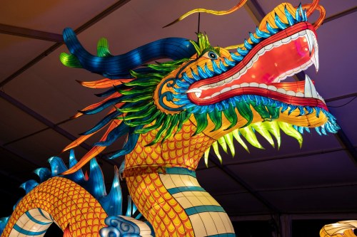 A vibrant, illuminated dragon lantern with colorful scales and a fierce expression, displayed indoors.