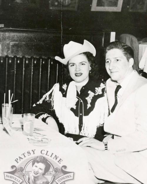 A vintage black-and-white photo of a woman in a cowboy hat and a man in a suit, sitting at a table with drinks.