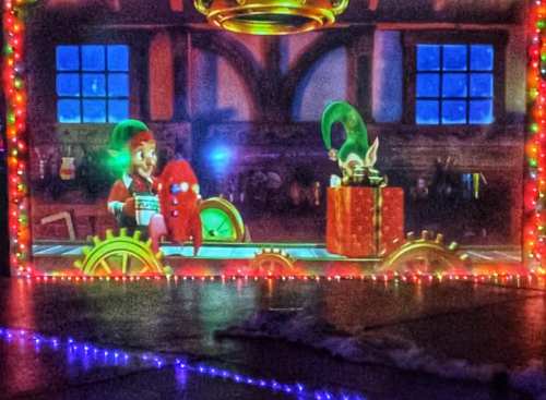 A colorful animated scene with characters on a train, surrounded by festive lights and a cozy interior backdrop.
