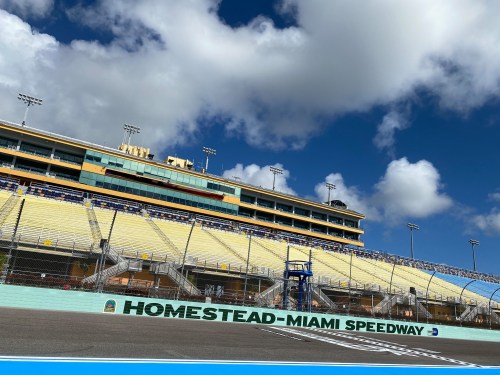 View of Homestead-Miami Speedway with grandstands under a blue sky and scattered clouds.