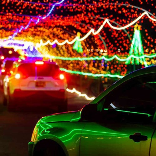 A car drives through a colorful light display with vibrant blue, green, and red lights illuminating the scene.