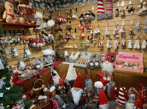 A festive display of holiday decorations, including gnomes, ornaments, and various Christmas-themed items on wooden shelves.