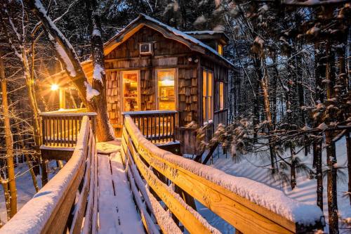 A cozy treehouse illuminated at night, surrounded by snow-covered trees and a wooden walkway.