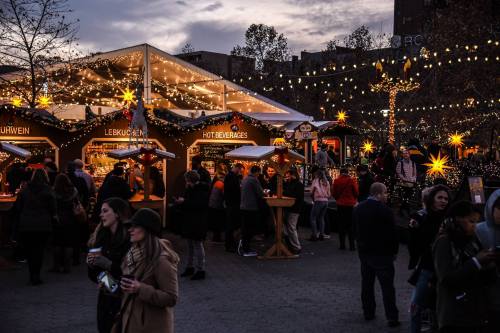 A festive market scene with people enjoying food and drinks under twinkling lights and a large tent.