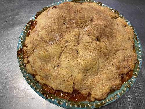 A freshly baked pie with a golden-brown crust, sprinkled with cinnamon, in a decorative blue dish.