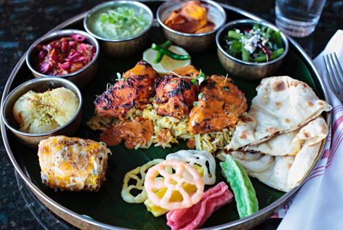 A vibrant platter of Indian cuisine featuring grilled chicken, rice, various sides, and naan bread, served on a banana leaf.