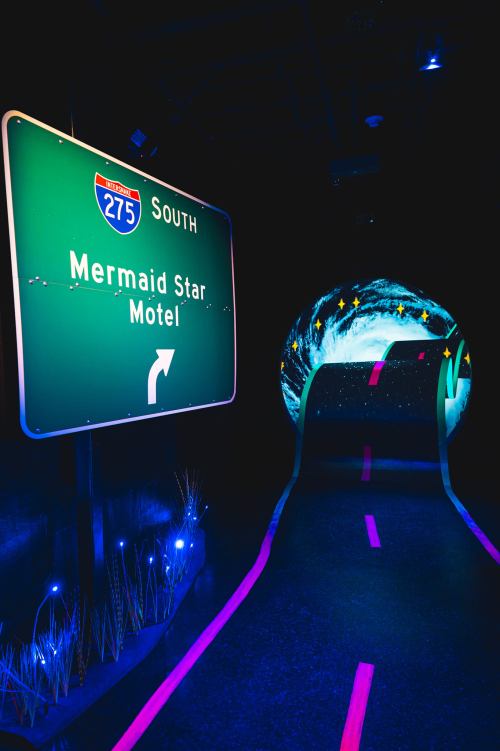 A glowing highway sign for "Mermaid Star Motel" leads into a colorful, starry tunnel.