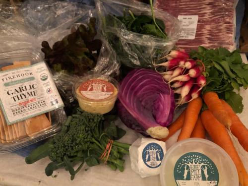 A variety of fresh vegetables and herbs, including radishes, carrots, lettuce, and garlic, arranged on a table.