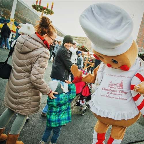 A woman and child interact with a gingerbread man mascot at a festive outdoor event.