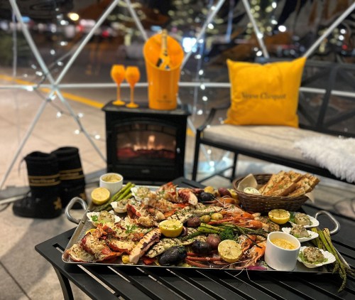 A beautifully arranged seafood platter with lemon, sides, and drinks, set in a cozy outdoor dining space.