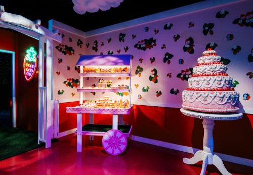A whimsical dessert display featuring a cake and a cart filled with sweets, set against a colorful, playful backdrop.
