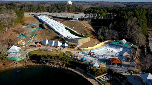 Aerial view of a water park with slides, a wave pool, and visitors enjoying the attractions surrounded by trees.