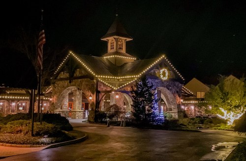 A beautifully lit building at night, adorned with festive lights and decorations, surrounded by greenery.