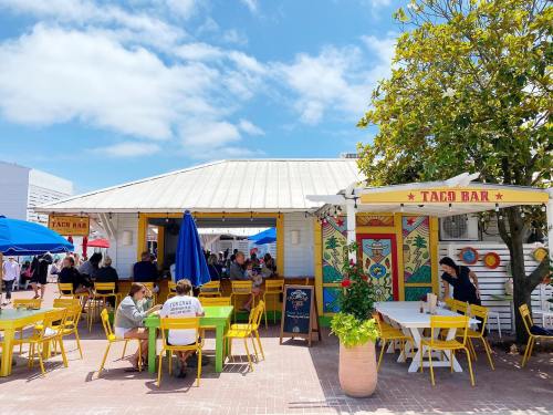 A vibrant outdoor taco bar with colorful decor, tables, and people enjoying their meals under blue skies.
