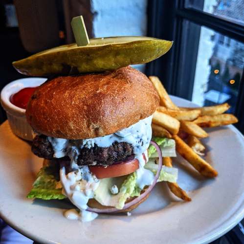 A juicy burger topped with lettuce, tomato, and sauce, served with fries and a side of ketchup. A pickle sits on top.