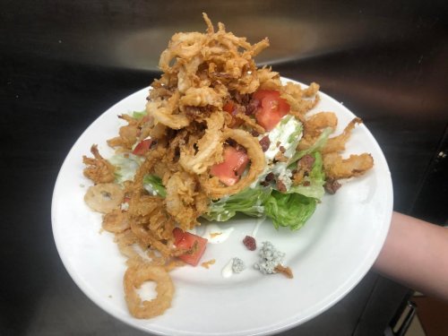 A plate of salad topped with crispy fried onions, tomatoes, and blue cheese on a bed of lettuce.