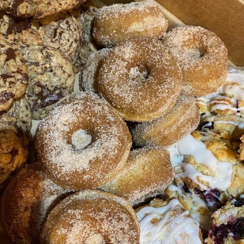 A box of assorted baked goods, including sugar-coated donuts and chocolate chip cookies.