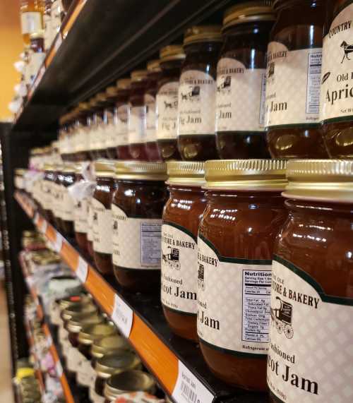 Shelves lined with jars of various fruit jams, including apricot and fig, in a grocery store.