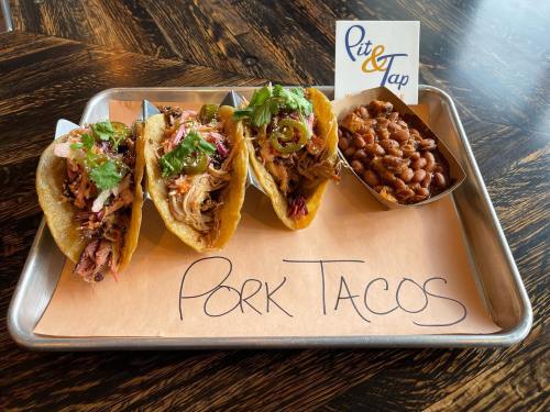 Three pork tacos topped with cilantro and jalapeños, served with a side of baked beans on a metal tray.