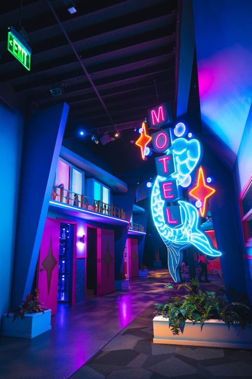 A vibrant motel entrance with neon signage and colorful lighting, featuring a fish design and a modern aesthetic.