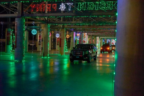 A dimly lit parking garage decorated with colorful holiday lights and cars driving through.