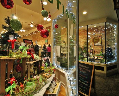 A festive shop window decorated with Christmas ornaments, lights, and greenery, showcasing holiday items inside.